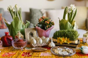 A vibrant arrangement of Nowruz haft-seen elements featuring greenery, flowers, and traditional items.