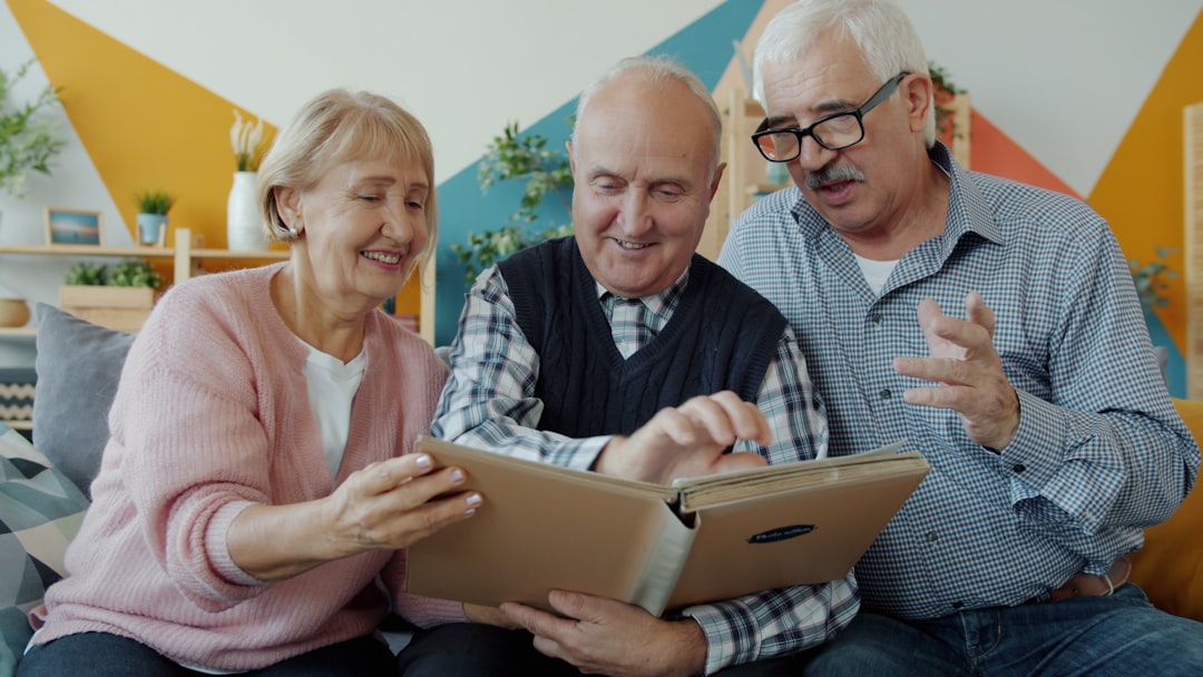 Retired men and woman watching photographs in photobook talking smiling enjoying recollections sitting on couch together. Friendship and communication concept.