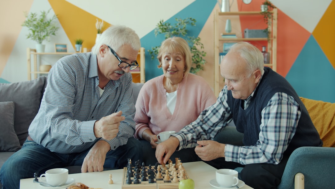 Happy retired men are playing chess game while cheerful senior woman is watching and smiling relaxing in free time. Happiness and friendship concept.